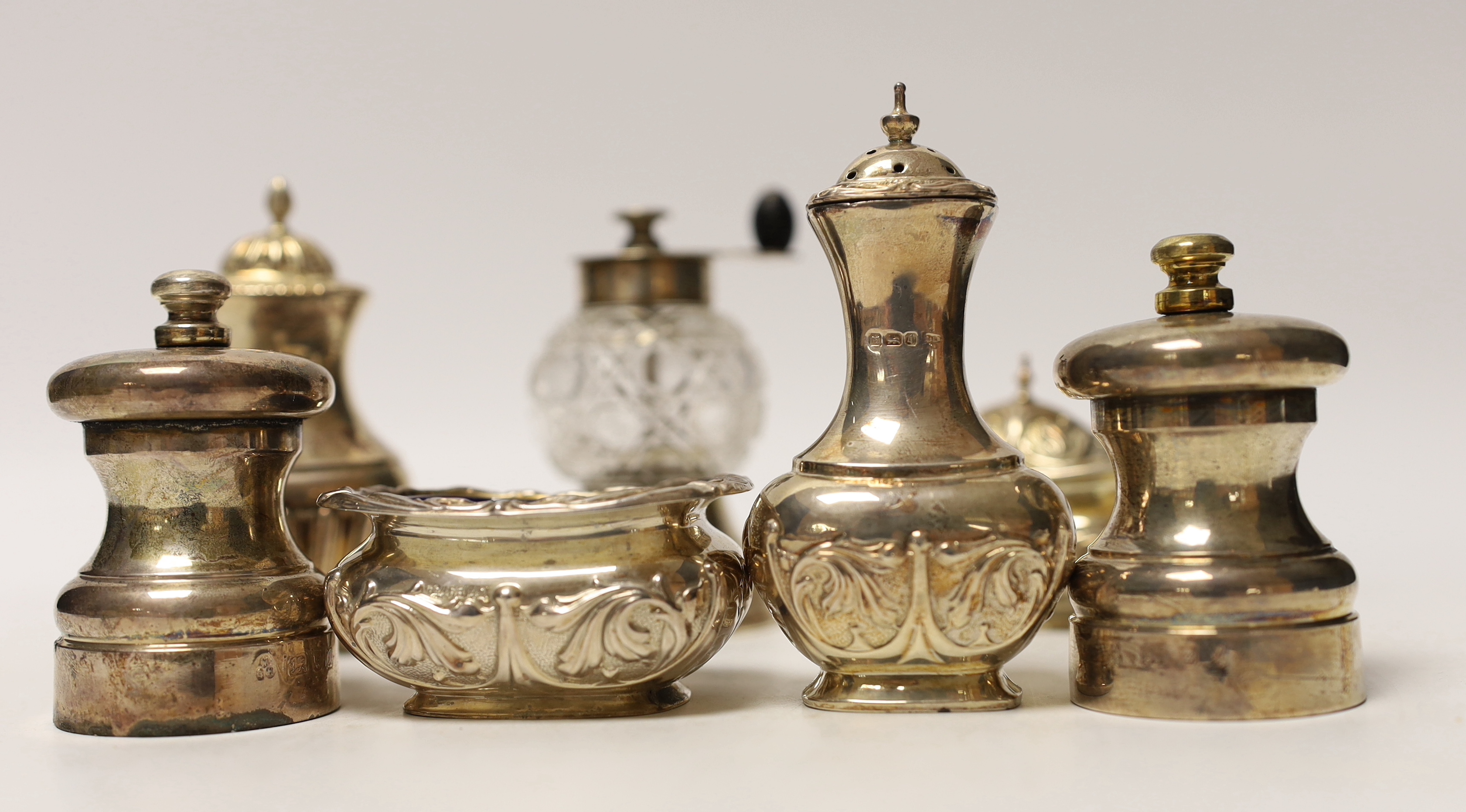 Seven assorted silver condiments, including a pepper grinder and salt and pepper mills.